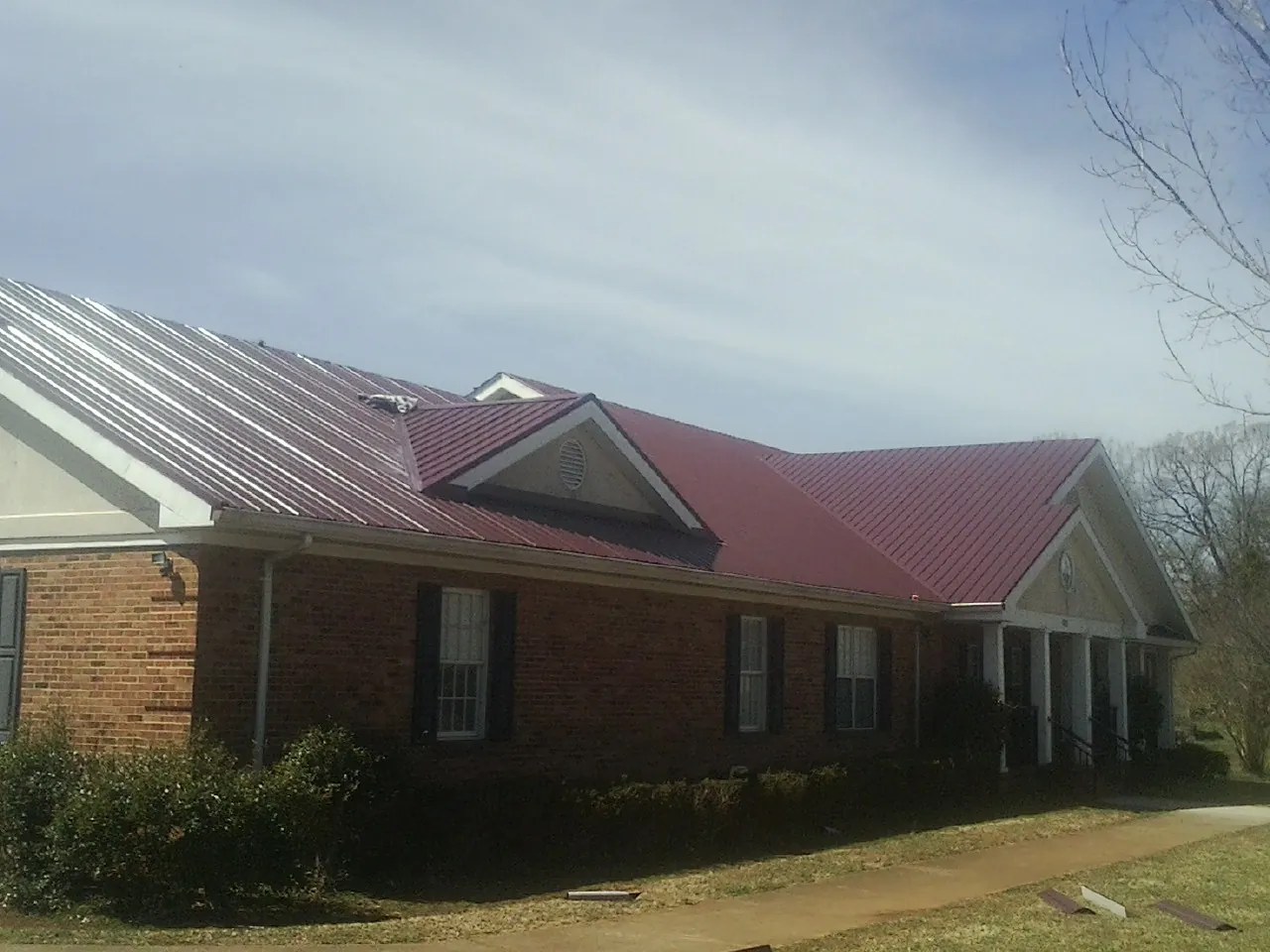 Red metal roof with gabled entries on a long brick building, from a Hail Damage Roof Repair job in Canterbury