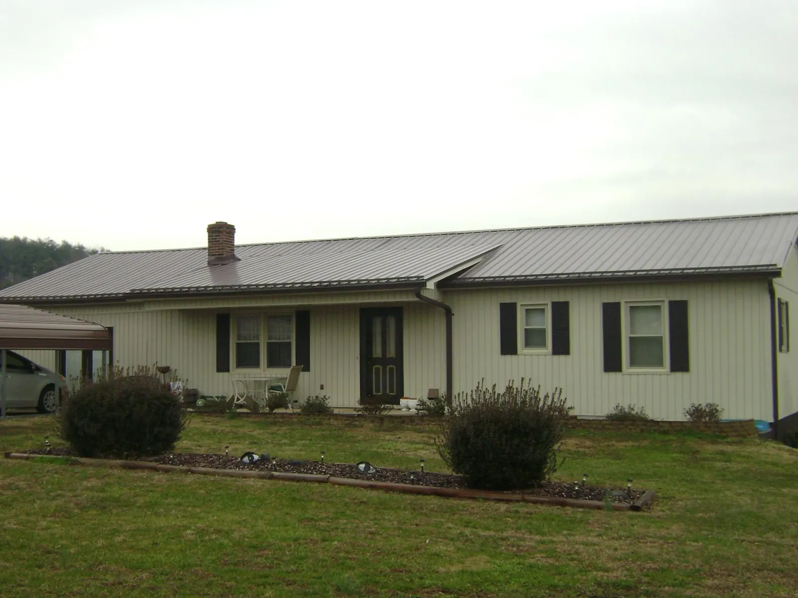 Brown metal roof on a cream sided ranch home with a brick chimney in Canterbury