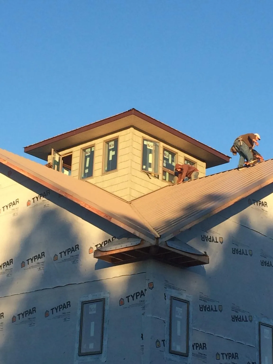 Roofers working around a rooftop cupola on a new metal roof at sunset — Roof Waterproofing in Canterbury by Roofing Brothers